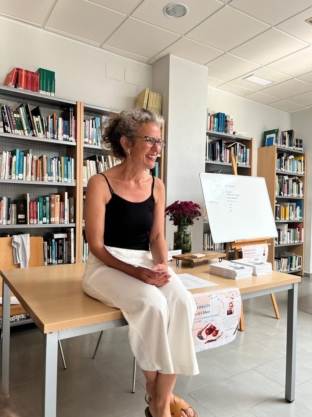 Reyes Andreo sonriendo, sentada en una mesa de la biblioteca durante la presentación de su libro