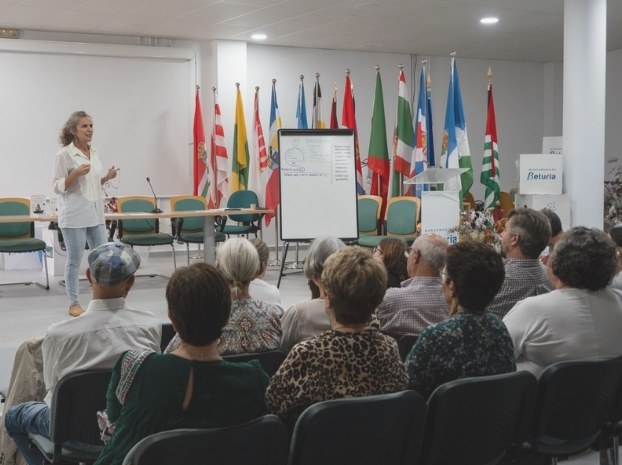 Reyes Andreo hablando ante un grupo, con banderas al fondo