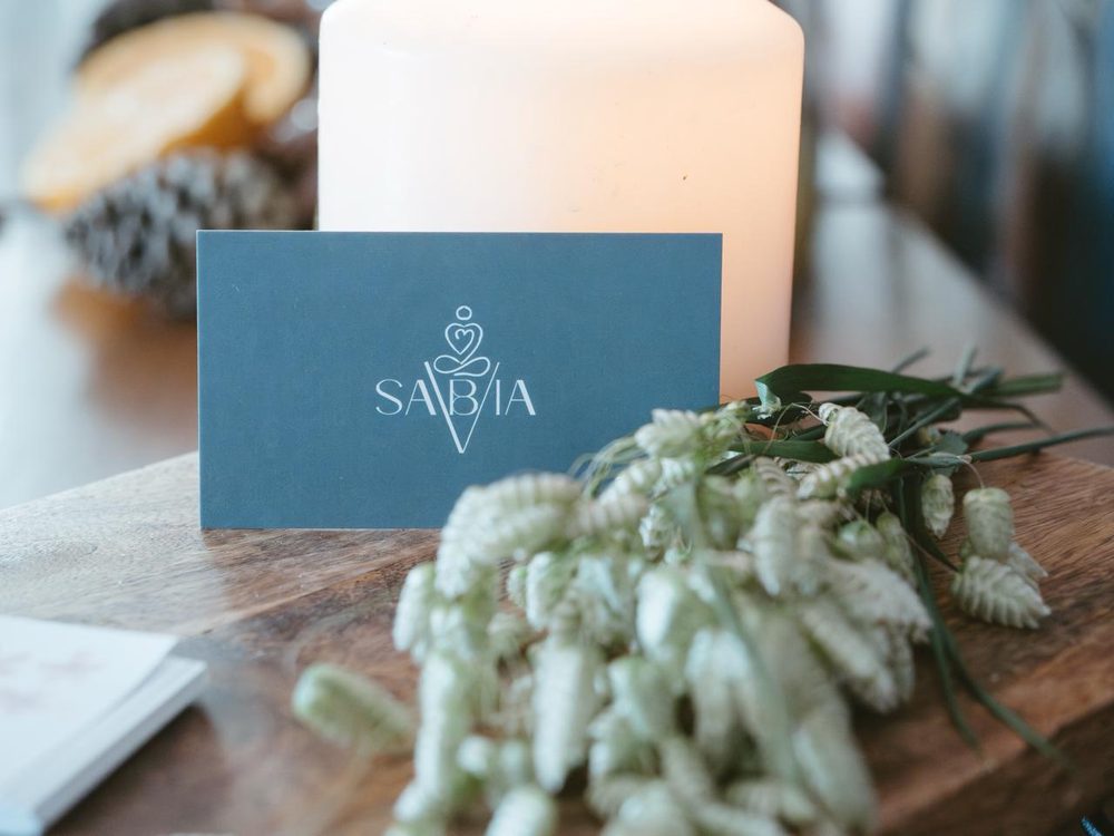 Tarjeta de Sabía Eventos junto a una vela y flores secas